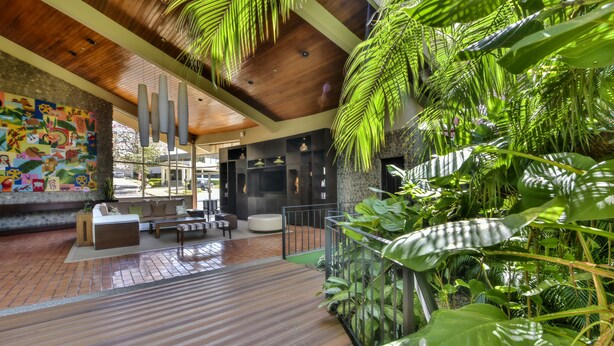 A modern interior with a wooden ceiling, a colorful mural, a seating area, and lush green plants. - DoubleTree by Hilton Cariari - San Jose Costa Rica (La Asunción)