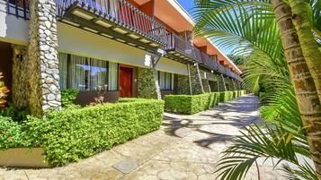 Un hotel con fachada de piedra, un corredor cubierto y abundante vegetación bien cuidada.