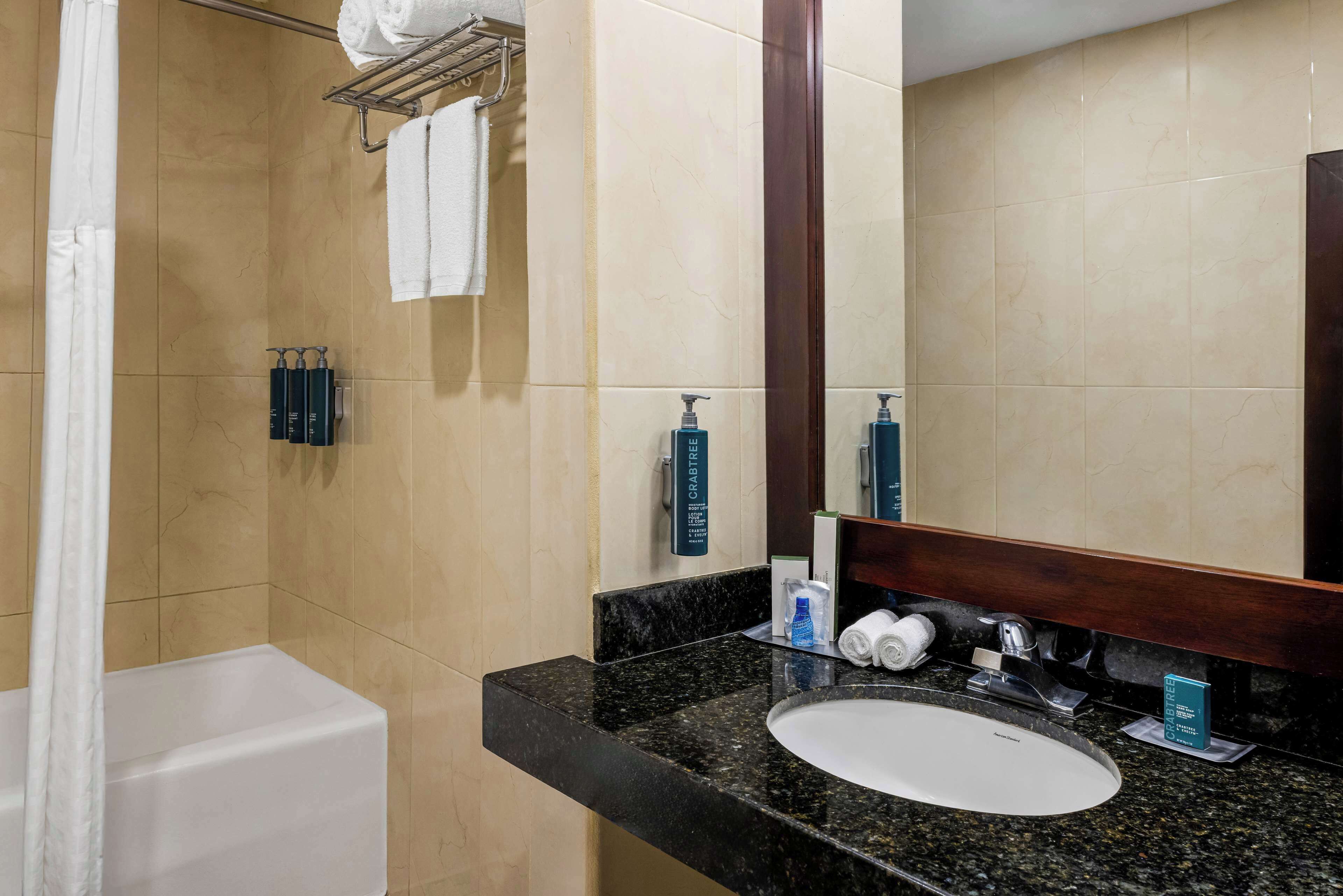 Um banheiro com banheira branca, bancada de granito preto, pia branca e um espelho grande.