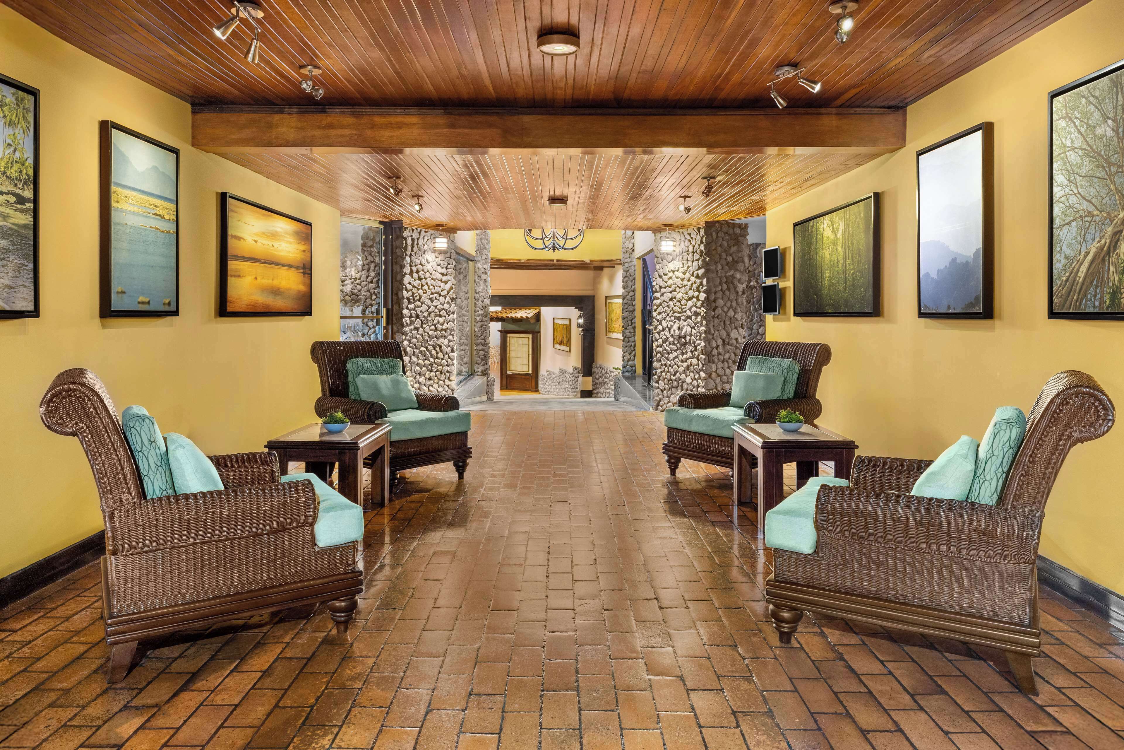 A lobby with two wicker sofas, a brick floor, wooden ceiling, and framed artwork on the walls.