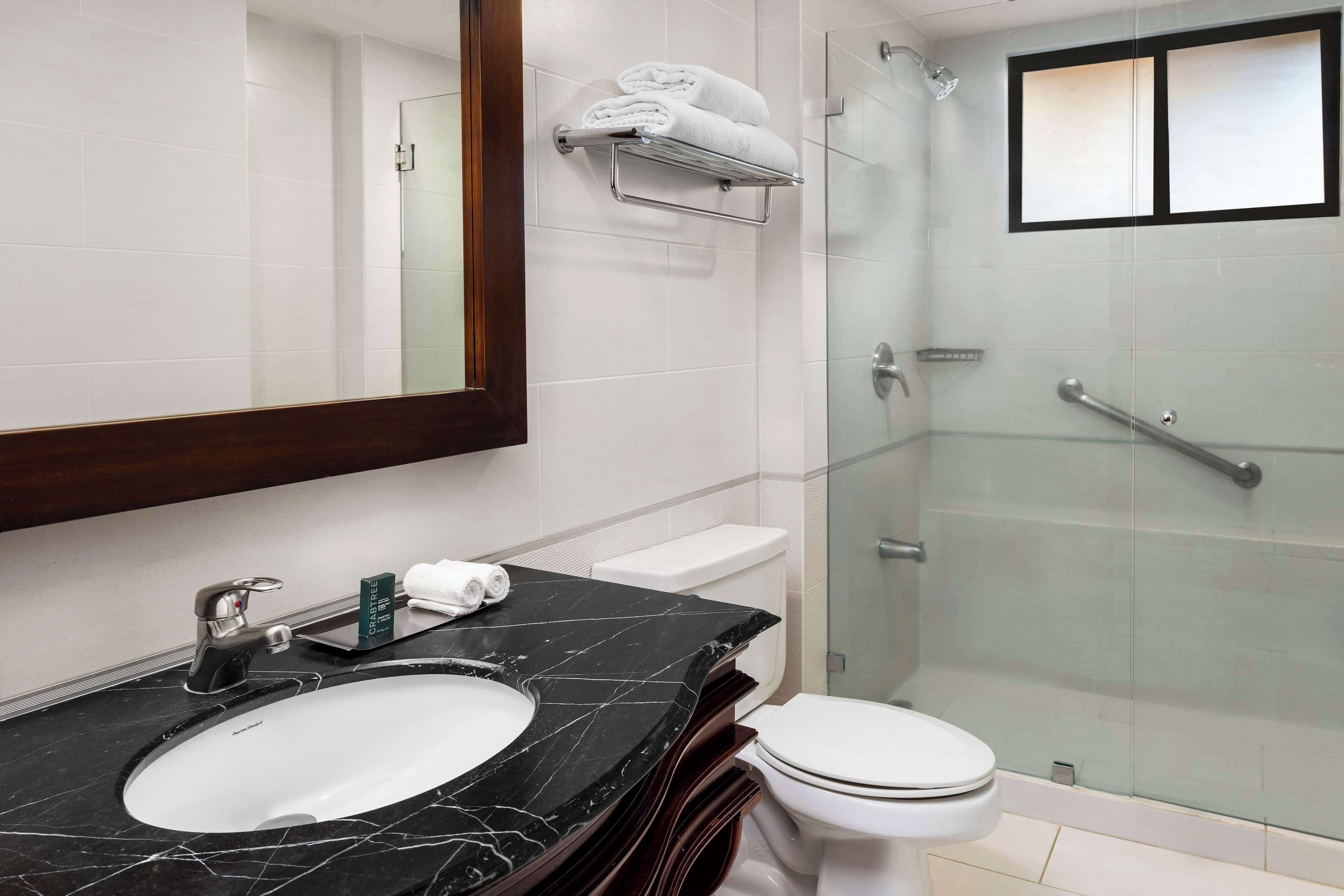 Un baño moderno con lavamanos de mármol, inodoro y ducha con mampara de vidrio.
