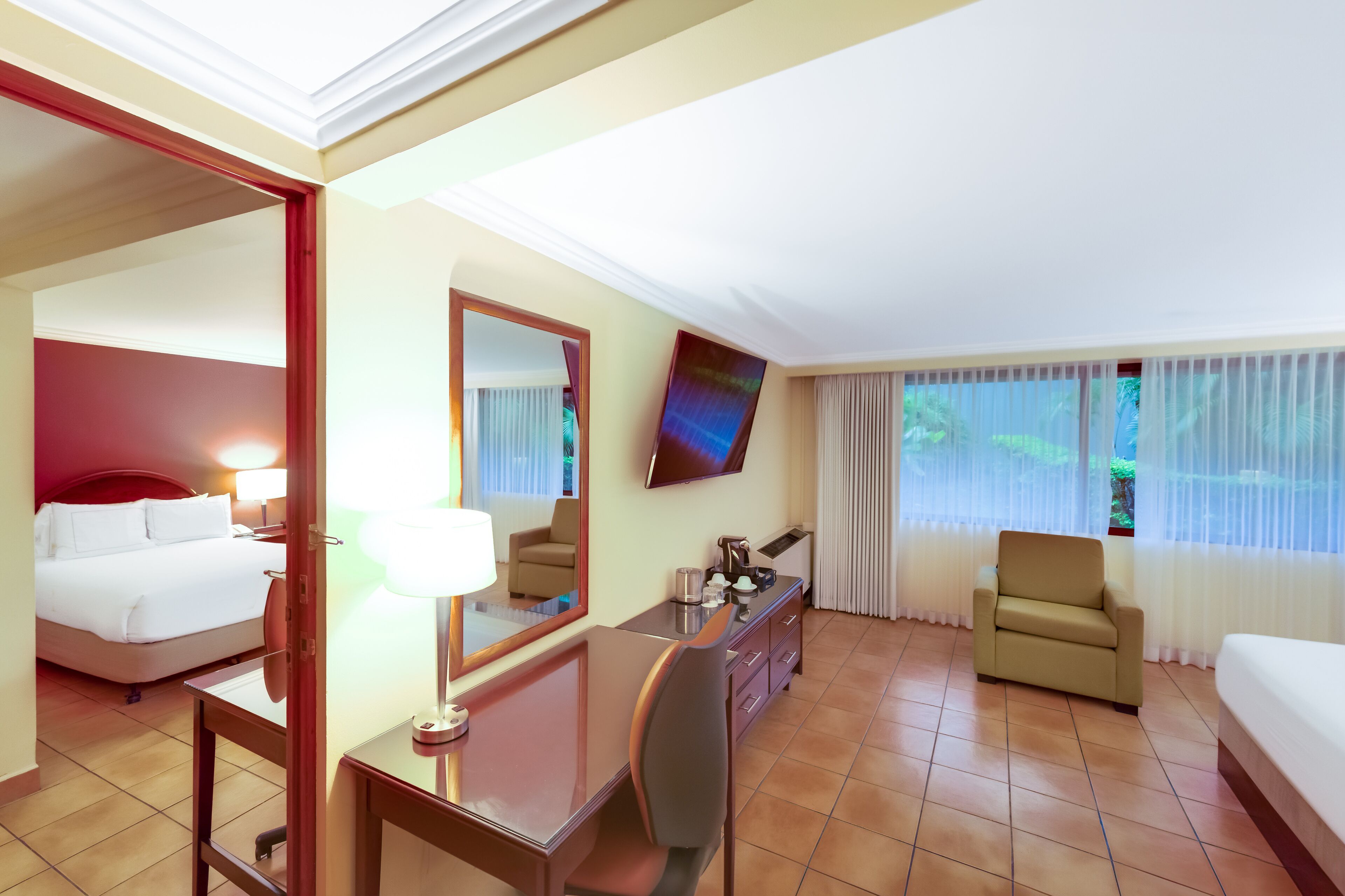 A hotel room with a bed, a desk, a chair, a TV, and a window with curtains.
