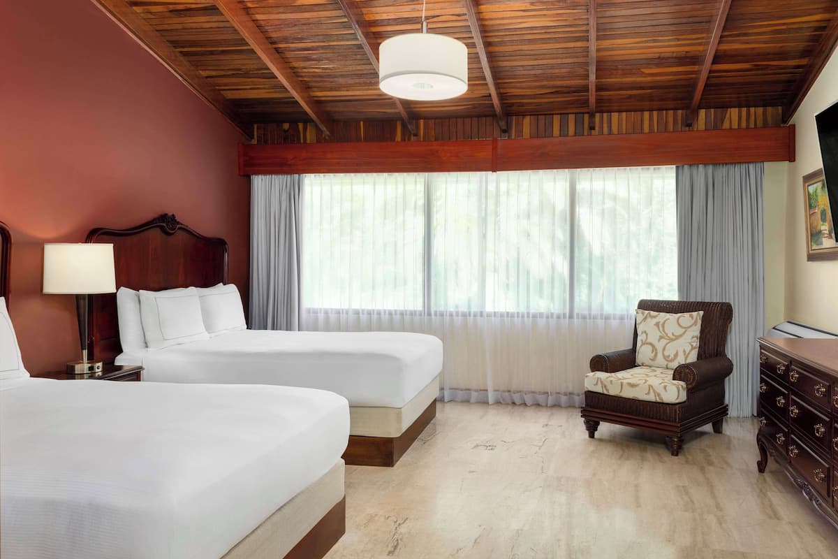 A hotel room with two beds, a wooden ceiling, a chair, and a dresser.