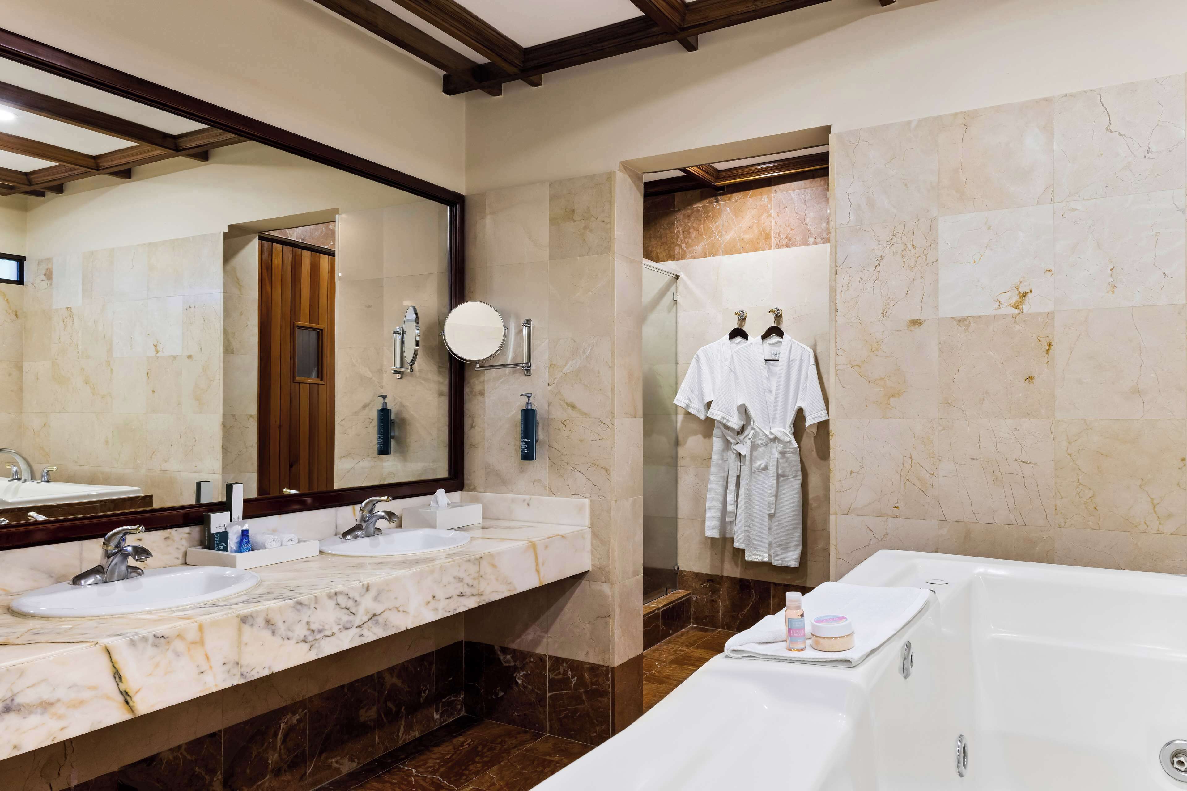 A modern bathroom with two sinks, a large mirror, a bathtub, and a shower area.