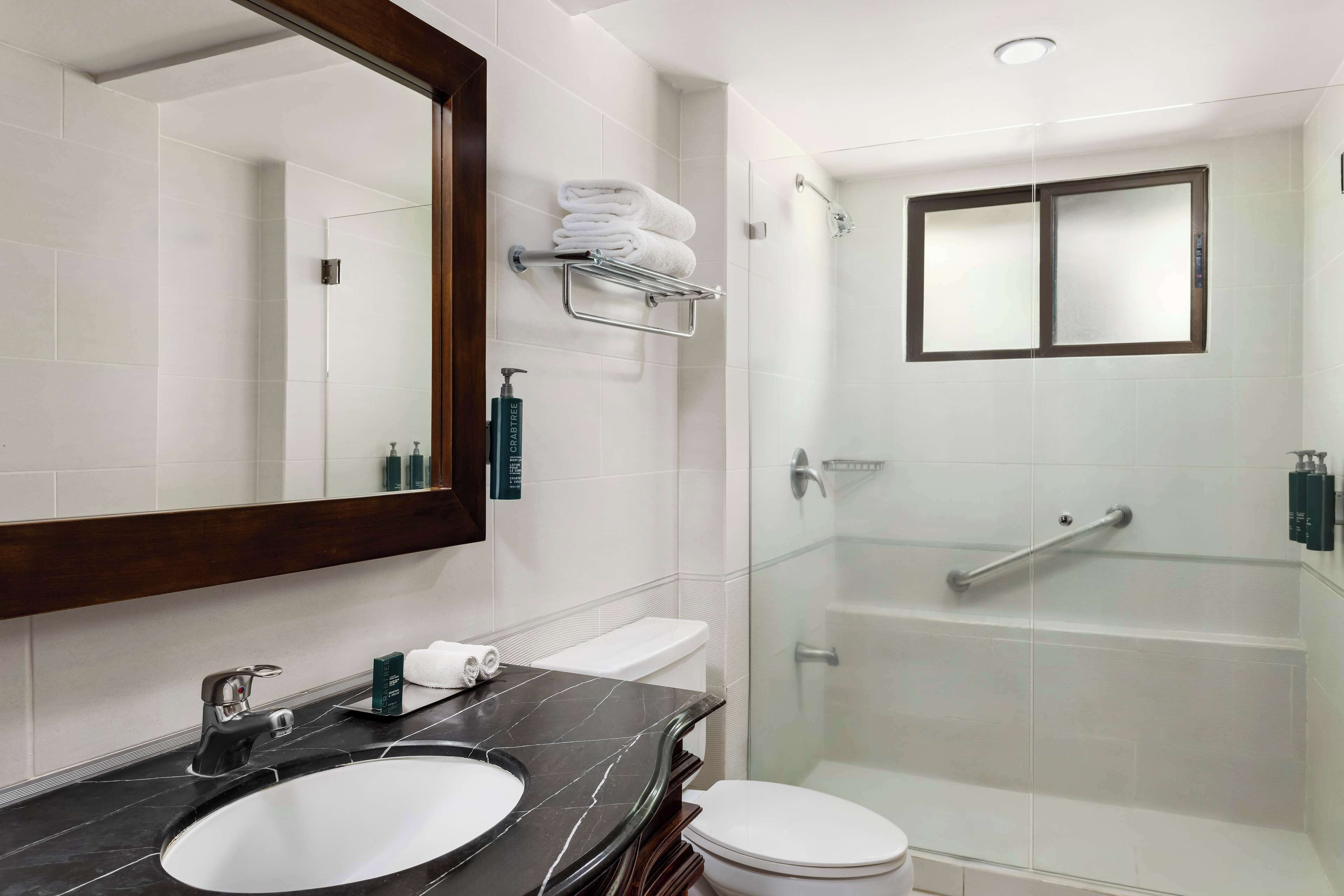 A modern bathroom with a large mirror, a black marble sink, a white toilet, and a glass-enclosed shower area.