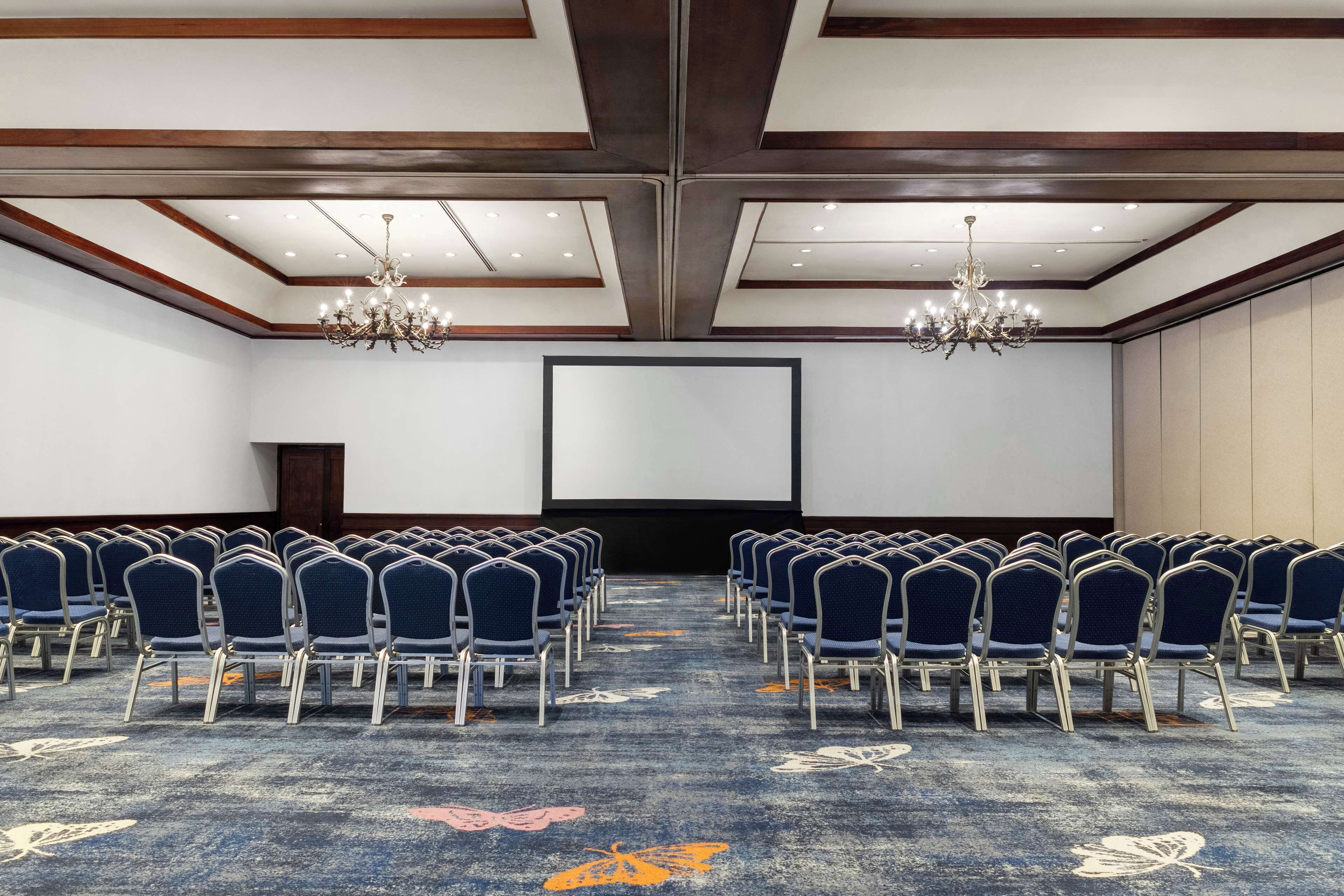 A conference room with rows of chairs, a large screen, and chandeliers.
