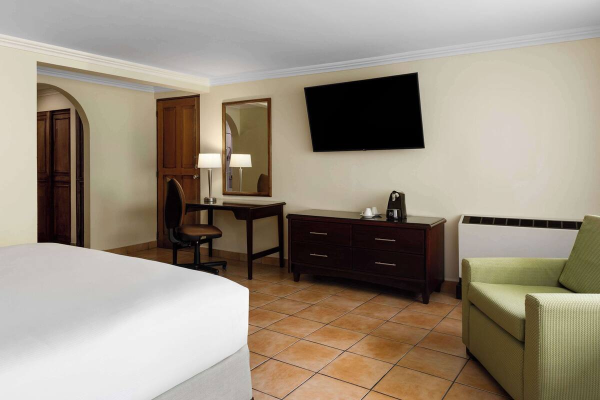 A hotel room with a bed, a desk with a chair, a dresser, a television, and a sofa.