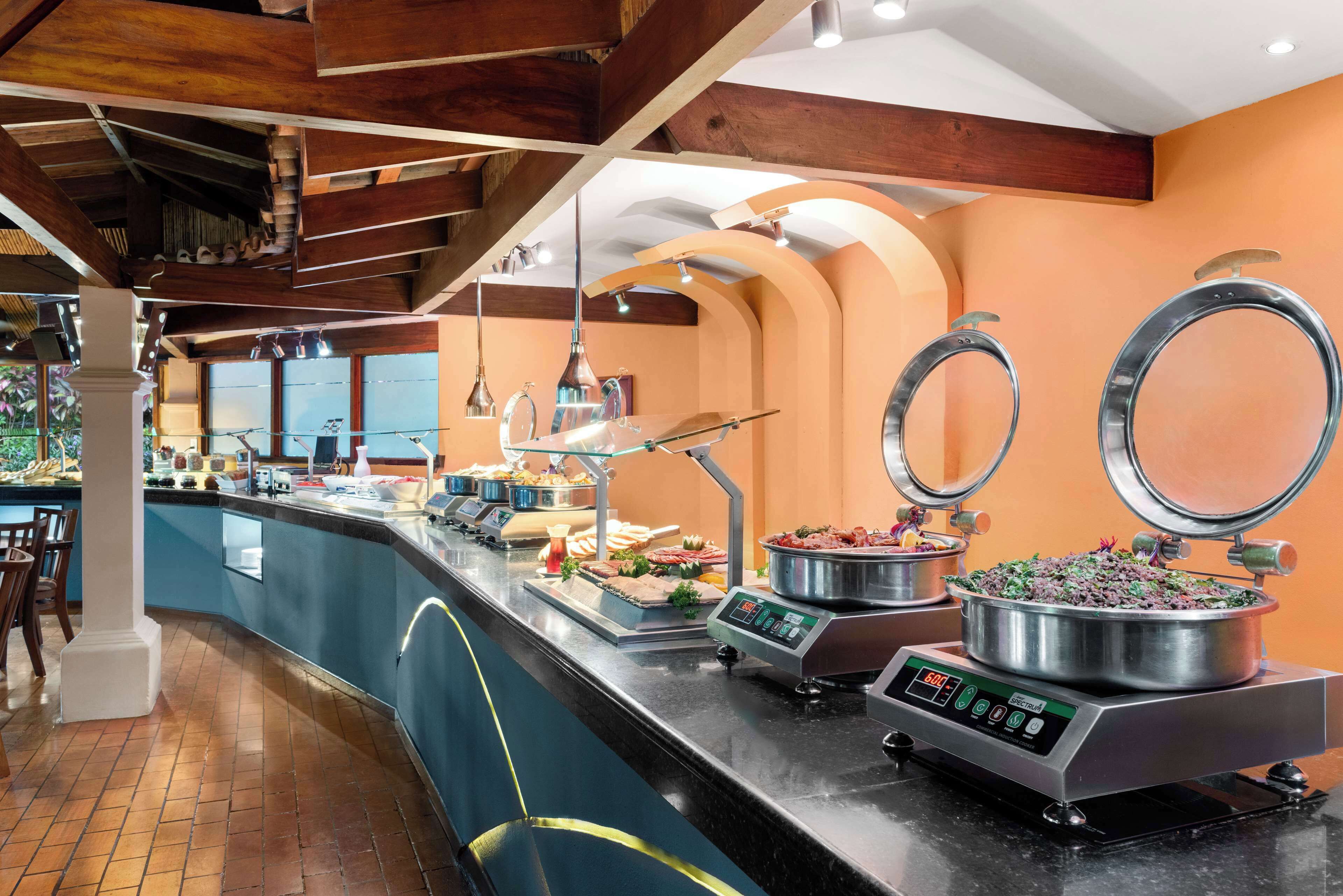 A buffet area with a variety of food items, a self-service beverage station, and a seating area with chairs.