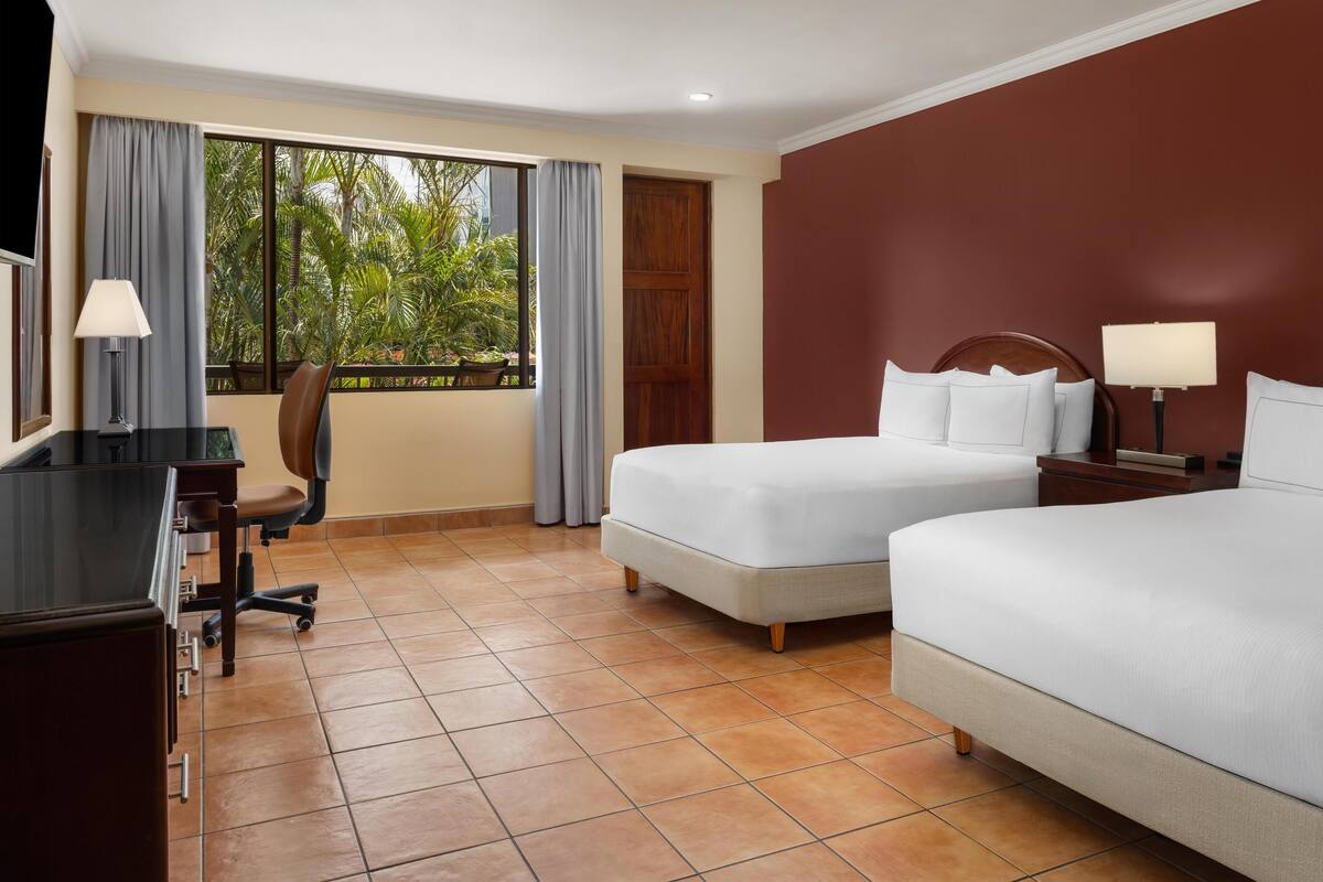A hotel room with two beds, a desk, and a chair.