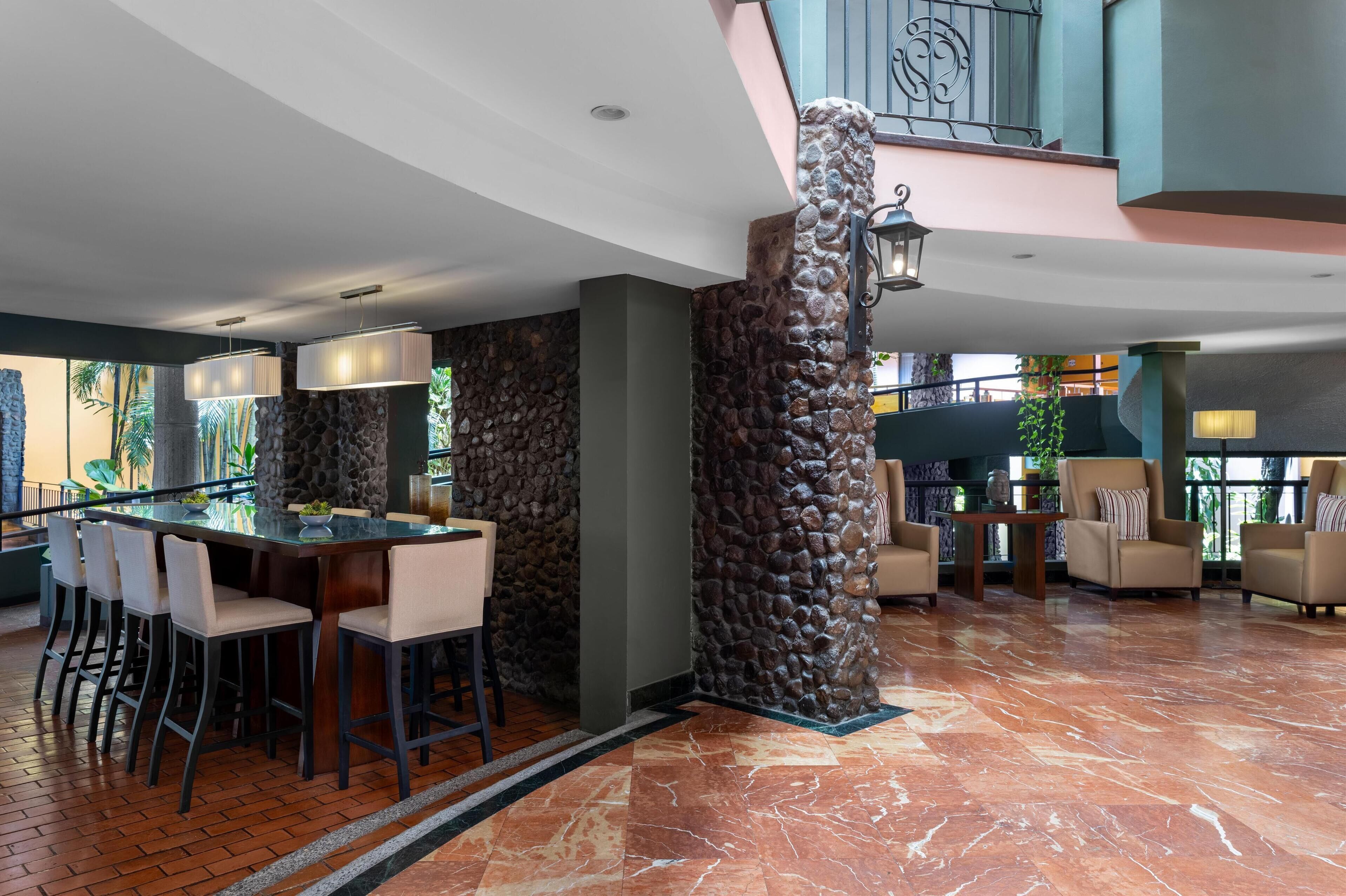 A modern lobby with a bar area, stone columns, and a staircase.