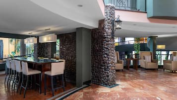 A modern lobby with a bar area, stone columns, and a staircase.