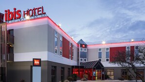 Een modern hotel met een opvallend 'ibis Hotel' bord, een goed verlichte ingang en een parkeerplaats.
