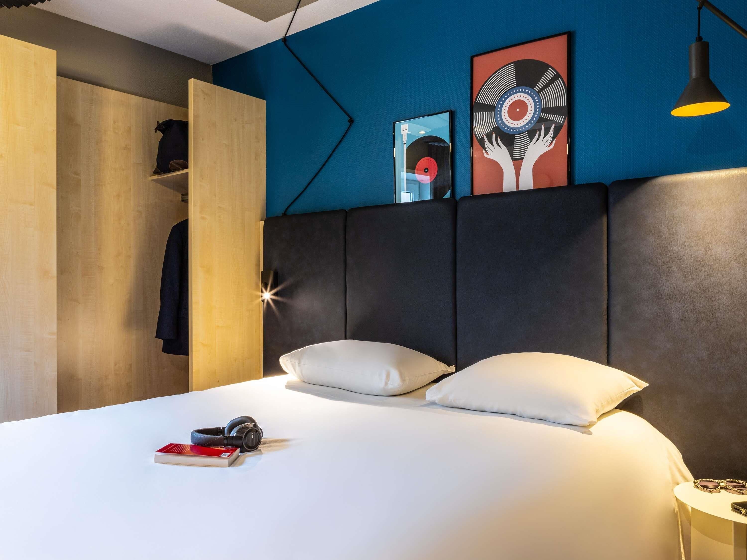 A modern bedroom with a bed, pillows, a bedside table, a lamp, and artwork on the wall.