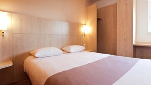 Une chambre d’hôtel moderne avec un grand lit, deux tables de chevet et une tête de lit en bois.