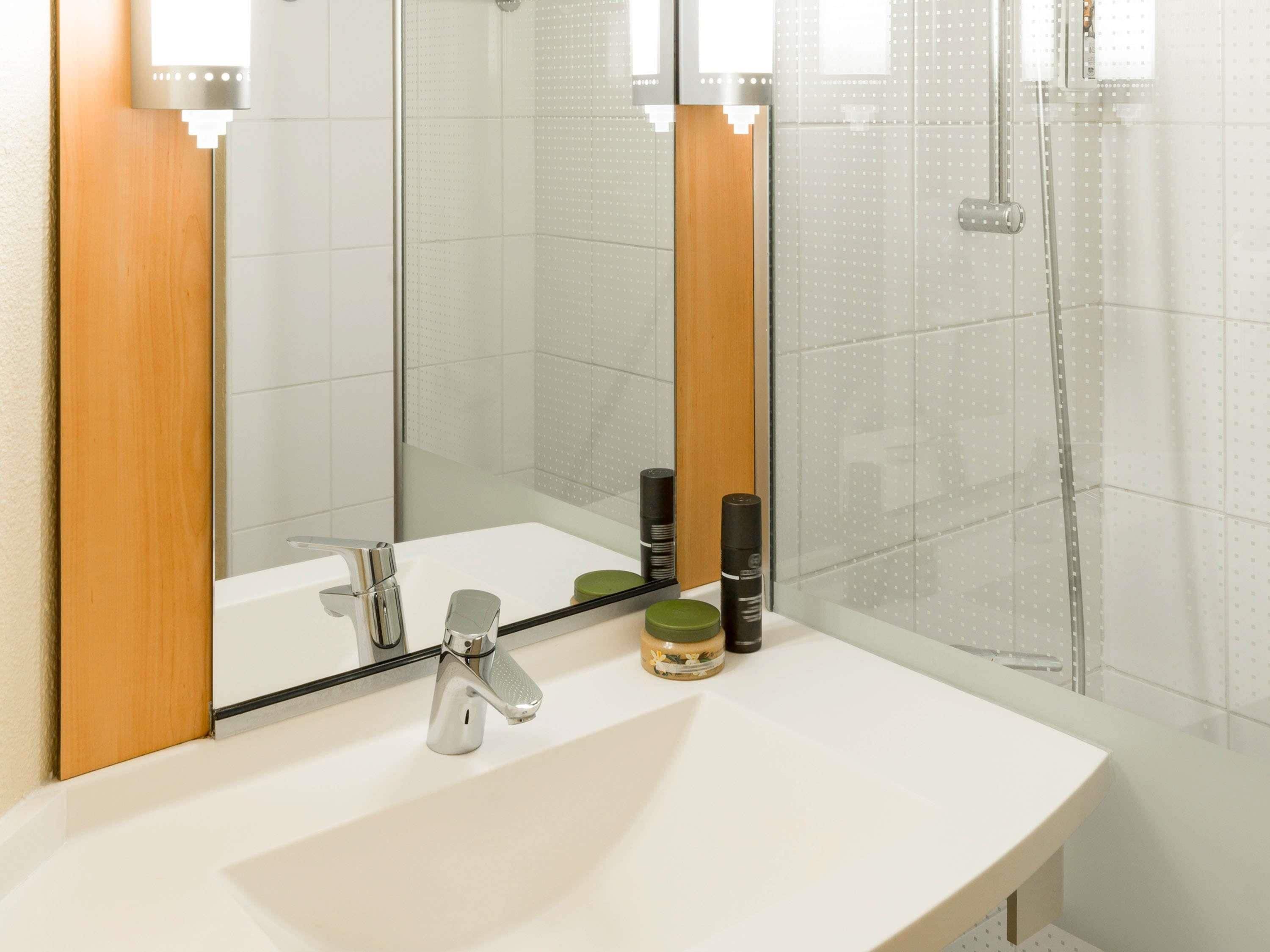 Un baño con lavamanos blanco, espejo y zona de ducha.