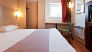 Une chambre d’hôtel équipée d’un lit, d’un bureau, d’une chaise, d’une fenêtre avec des rideaux et d’un téléviseur fixé au mur.