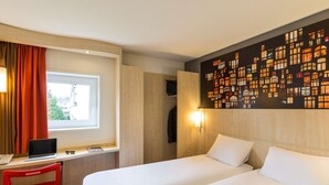 Une chambre d’hôtel avec deux lits, un bureau avec un ordinateur portable, une chaise rouge et une fenêtre avec des rideaux.