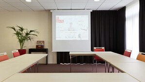 Une salle de conférence équipée d’un écran de projection diffusant une présentation, d’une plante en pot et d’un mur en briques.