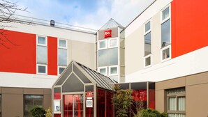Un hôtel moderne à la façade rouge et blanche, doté d’une entrée en verre et d’un petit jardin.