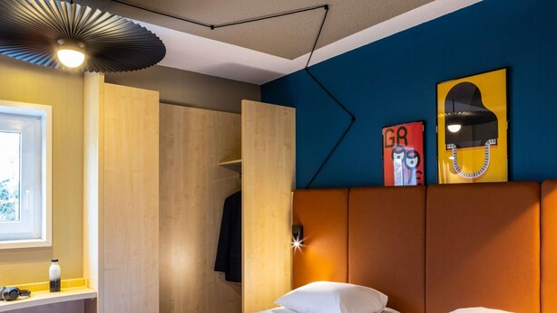 Une chambre d’hôtel avec un lit, une table de chevet, un miroir et une fenêtre.