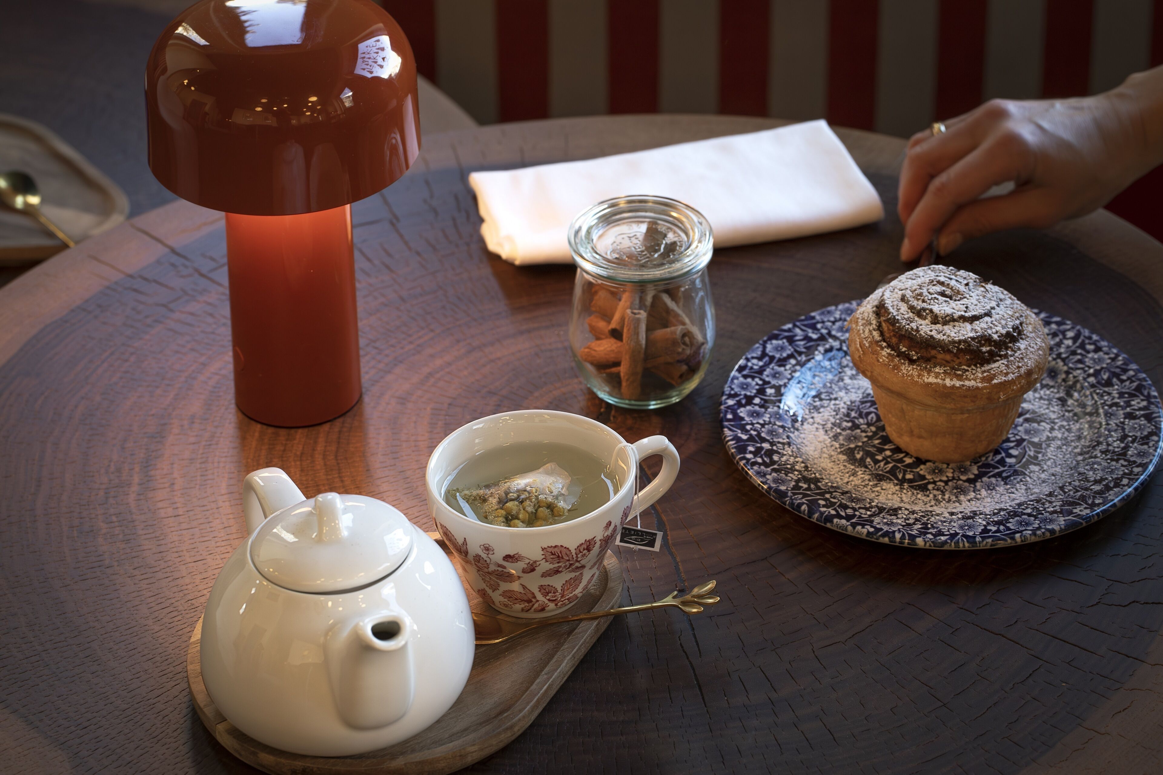 Una mesa con un calentador de agua, una taza de té, un muffin y una vela.