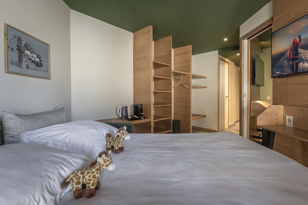 Une chambre avec deux lits, une armoire en bois, un bureau avec une bouilloire et un téléviseur fixé au mur.
