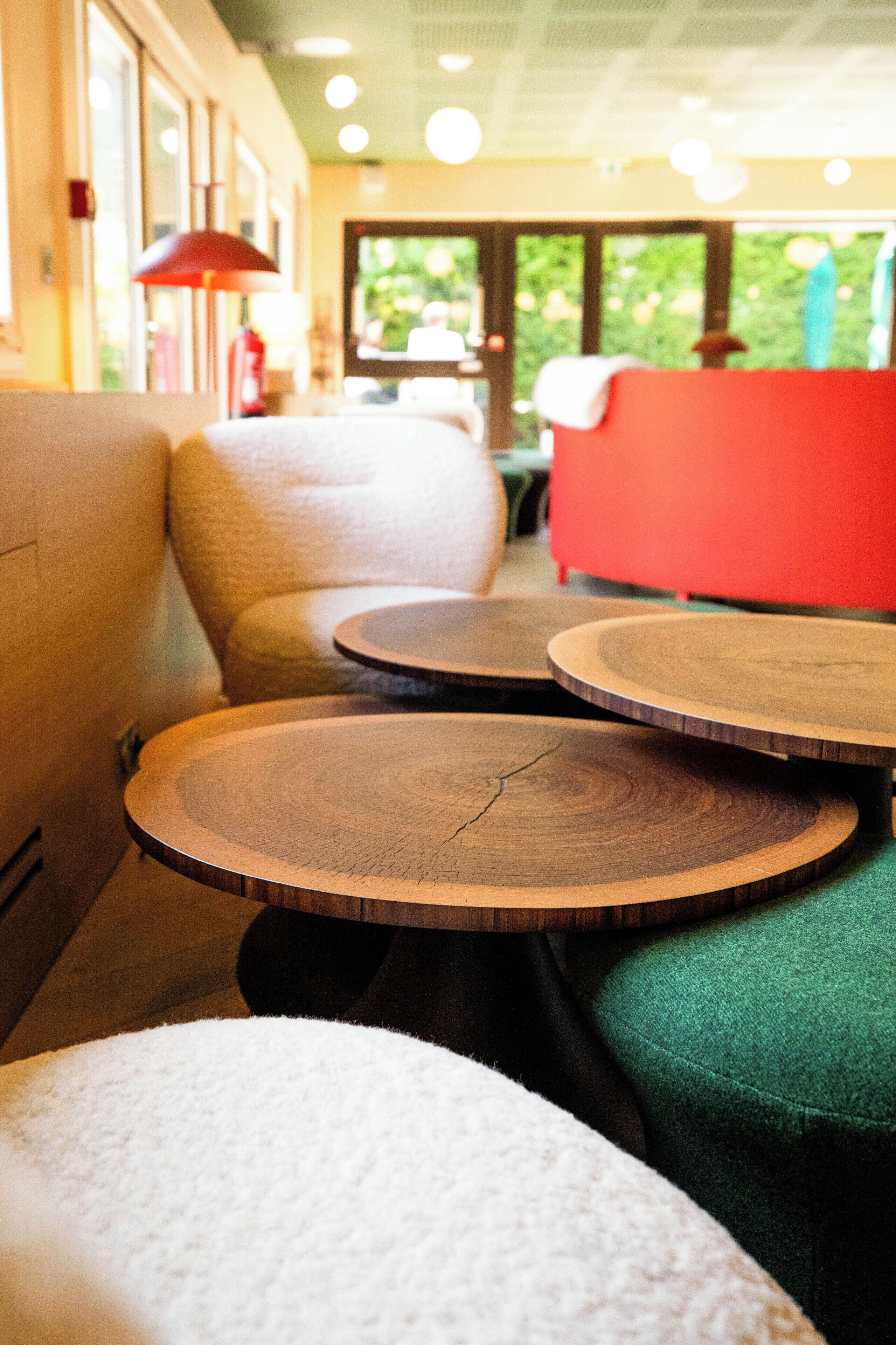 A seating area with round wooden tables and cushioned chairs, a red sofa, and a red lamp.