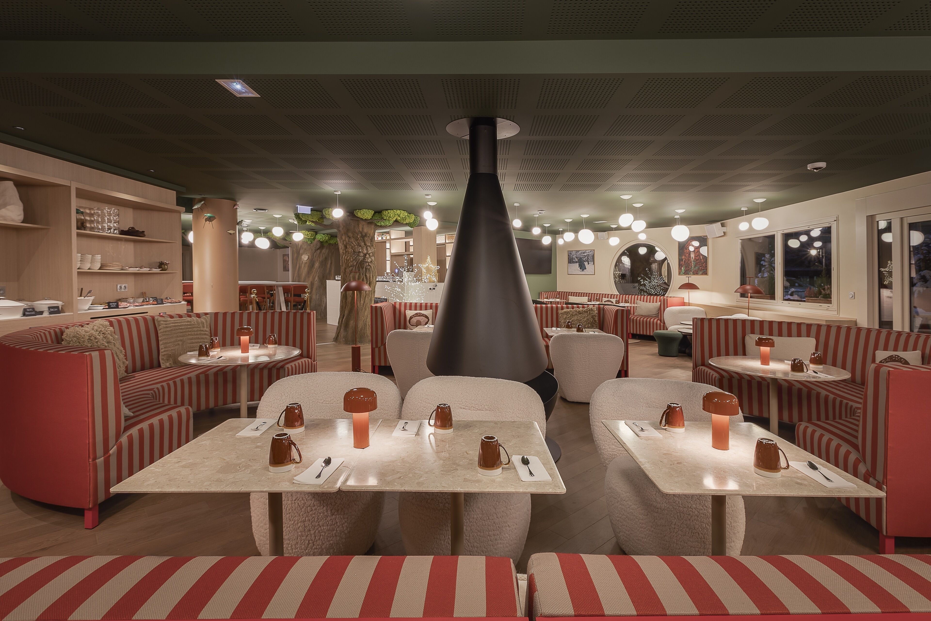 Um restaurante moderno com assentos listrados, mesas redondas e uma coluna preta central.