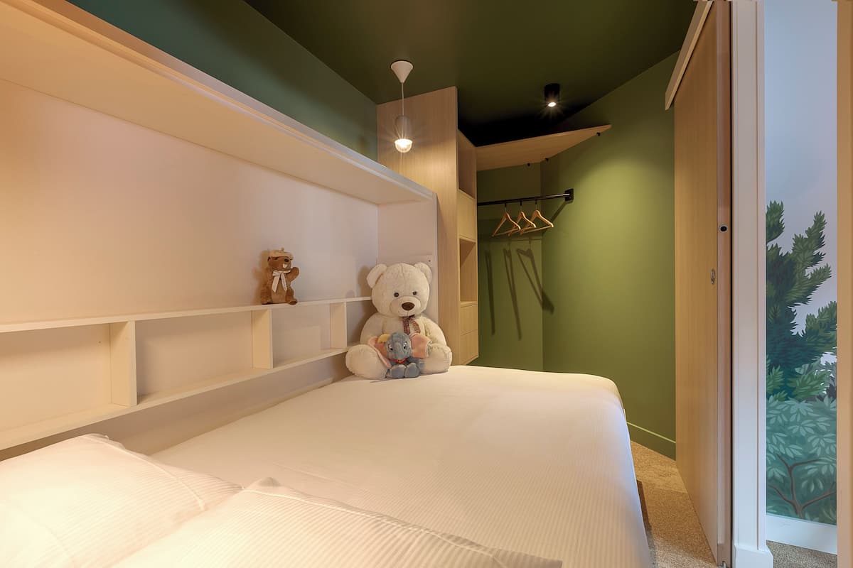 Une chambre à coucher avec un lit, une tête de lit blanche, un luminaire suspendu et une vue sur un arbre par la fenêtre.
