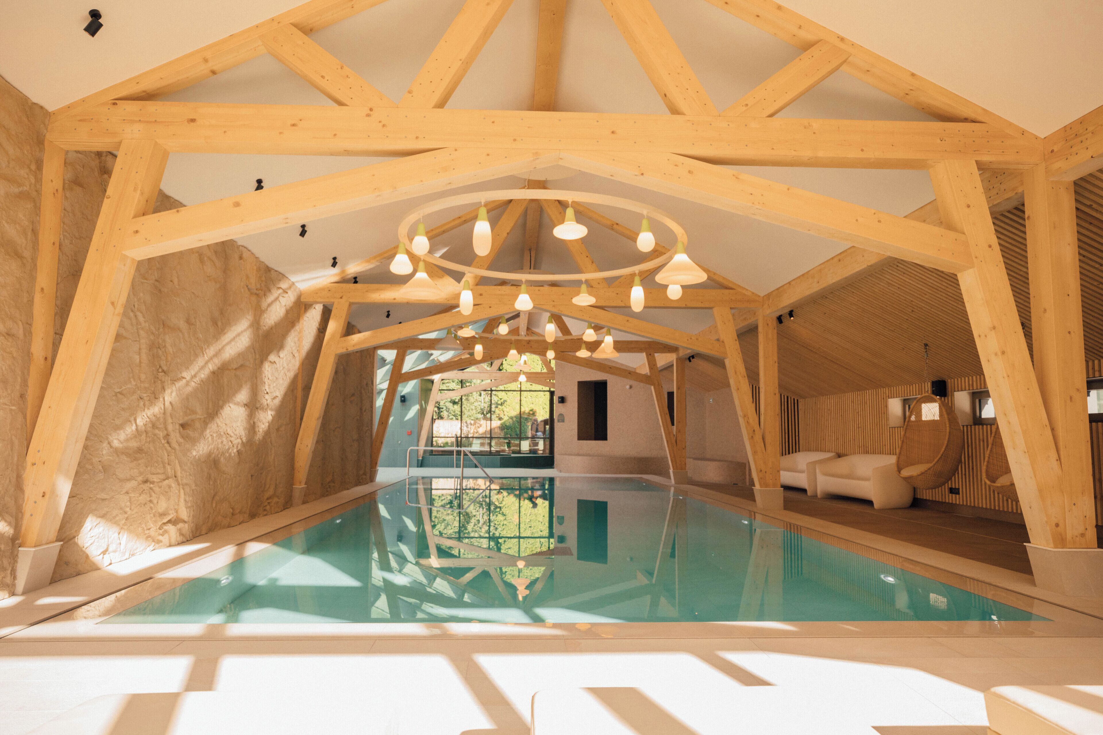 Una piscina interior con vigas de madera y un accesorio de luz circular.