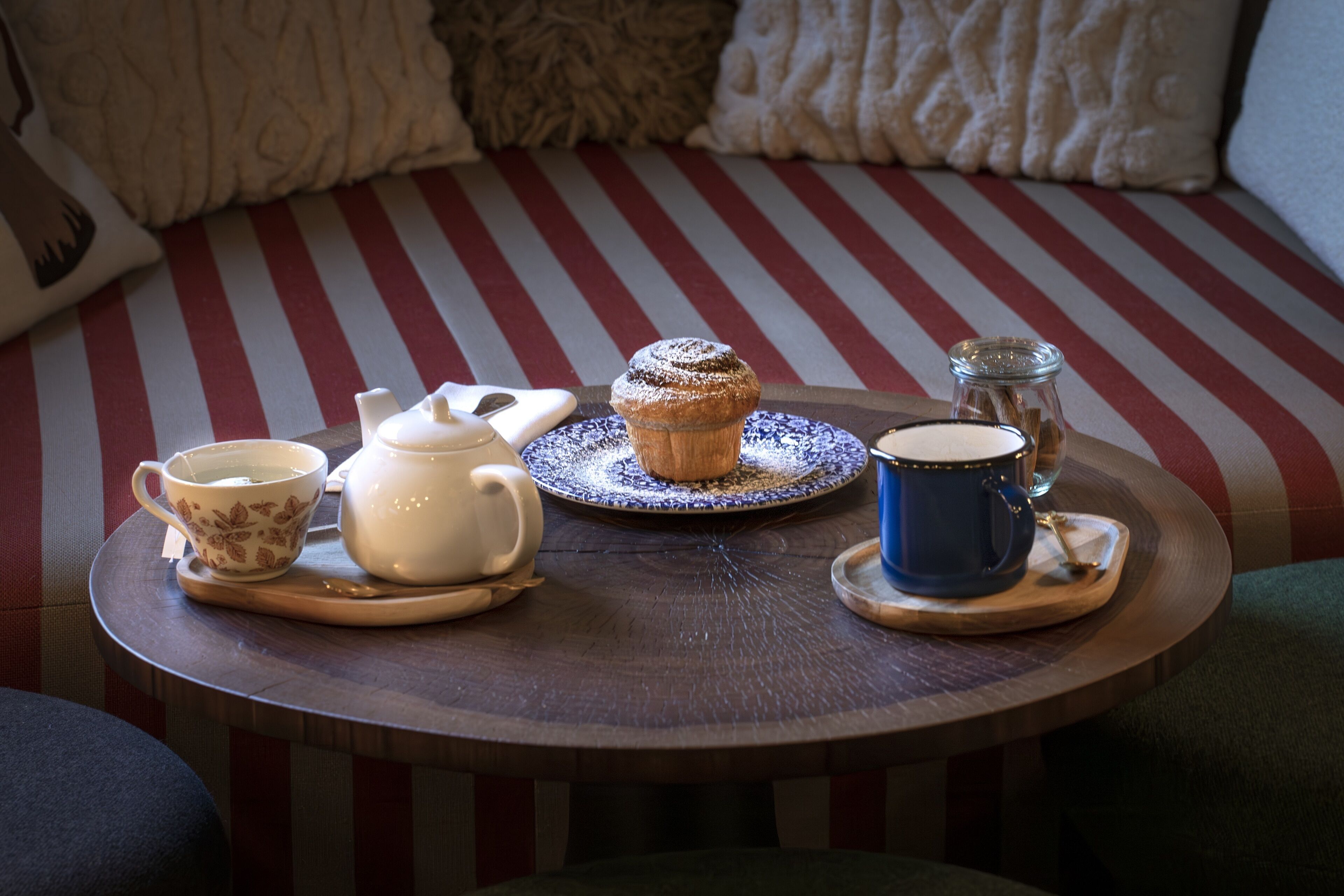 A round wooden table with a striped cushion in the background.