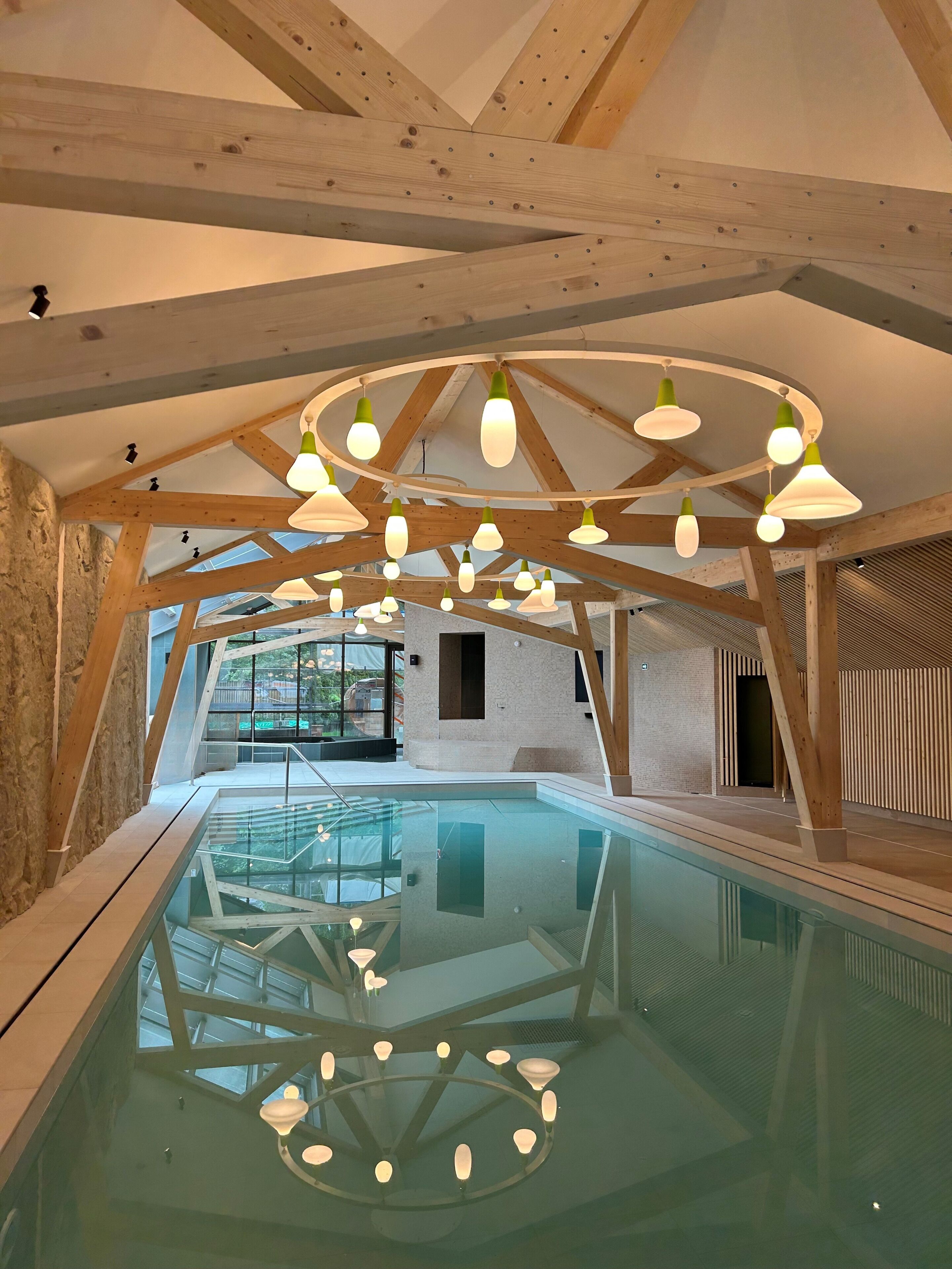 A modern indoor swimming pool with a glass ceiling and wooden beams.