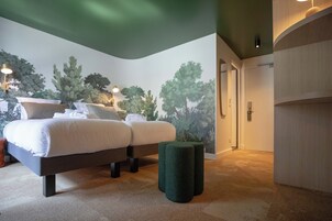 Un dormitorio con cama, almohadas, un reposapiés verde y un mural de árboles.