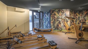 Une salle de remise en forme équipée de rameurs, d’un vélo d’appartement et ornée d’une fresque murale.