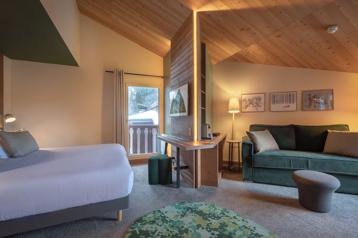 Une chambre d’hôtel avec un lit, un canapé vert, une petite table et un pouf vert.