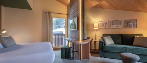 A hotel room with a bed, a green sofa, a small table, and a green ottoman.