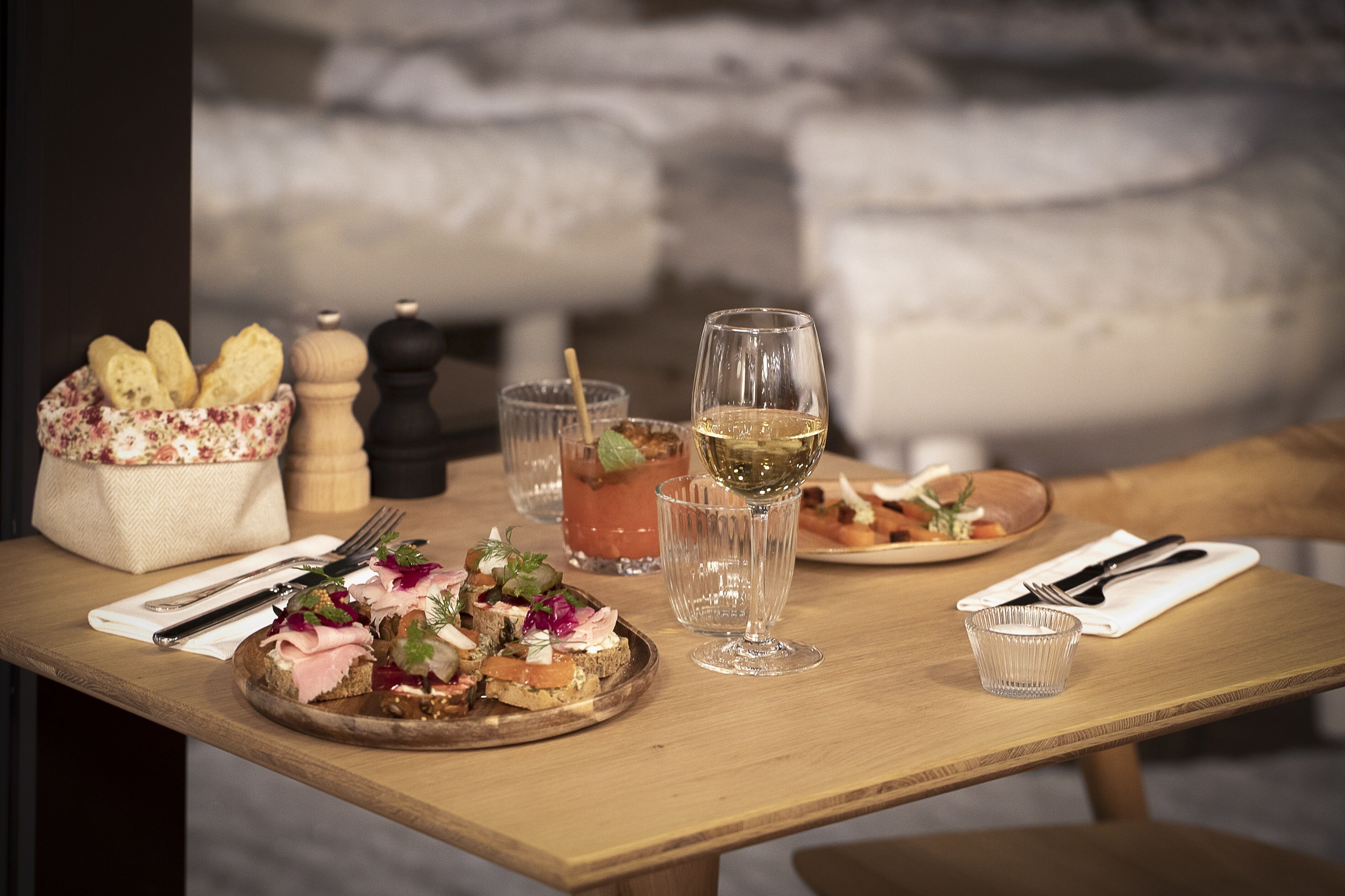 Una mesa de madera con diversos alimentos y bebidas, incluyendo pan, una copa de vino y un vaso pequeño de agua.