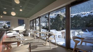 Un comedor moderno con amplios ventanales, mobiliario de madera y vistas a un paisaje nevado.