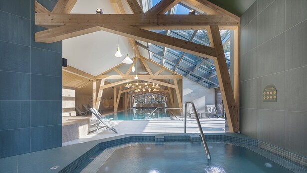 Una piscina interior con vigas de madera, techo de cristal y paredes de azulejos.