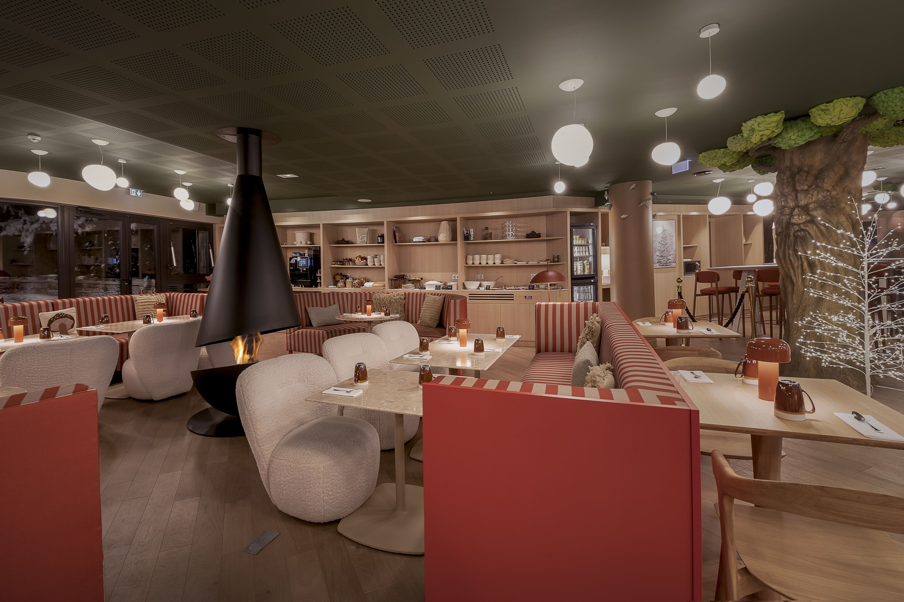 A modern restaurant with booths and tables, a central fire feature, and a tree decoration.