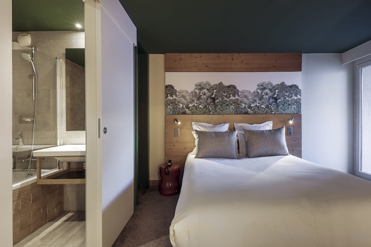 Une chambre à coucher avec un grand lit, une tête de lit en bois et un tableau représentant des arbres accroché au mur.