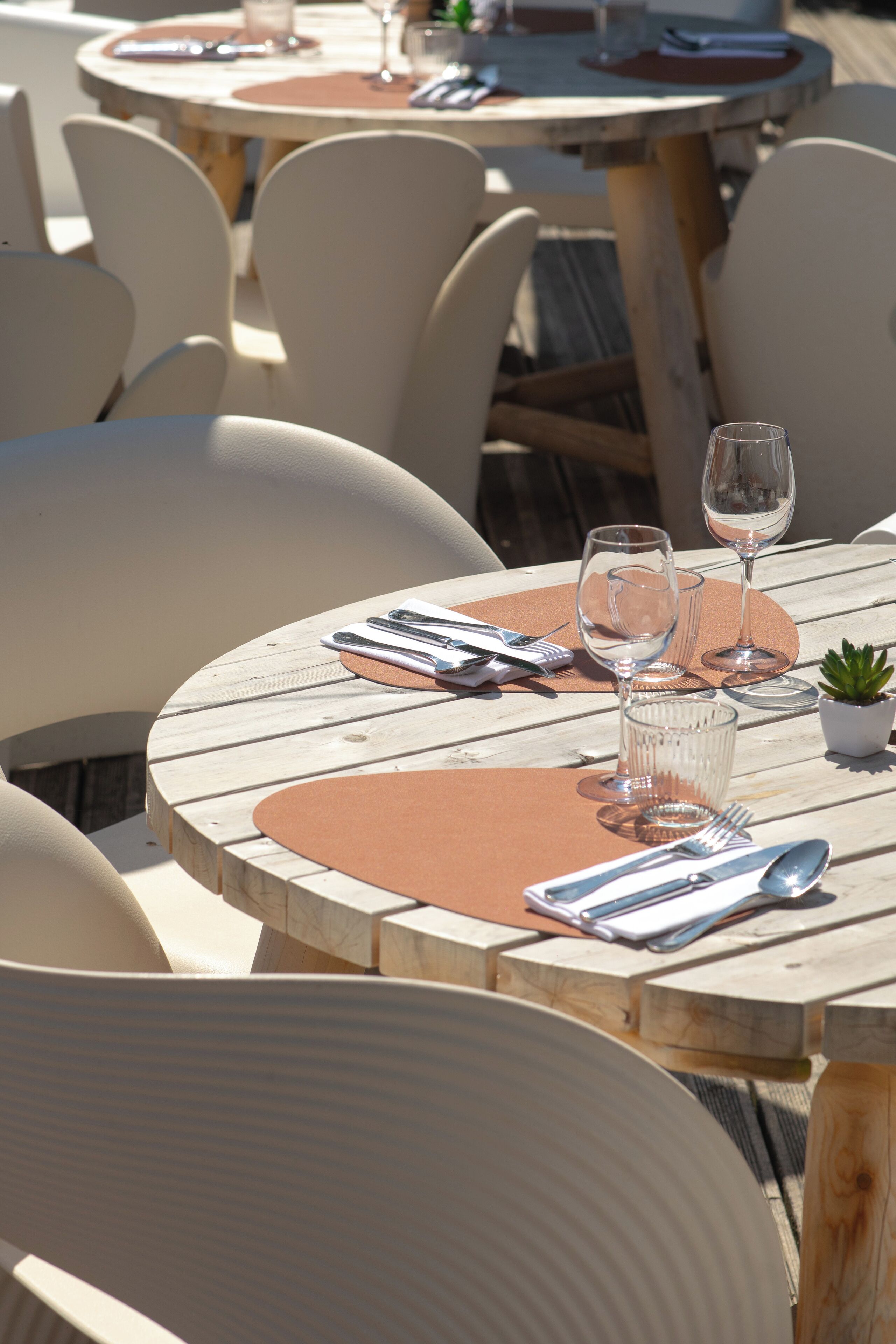 Une table ronde en bois, une chaise blanche, une petite plante en pot et des verres à vin vides.