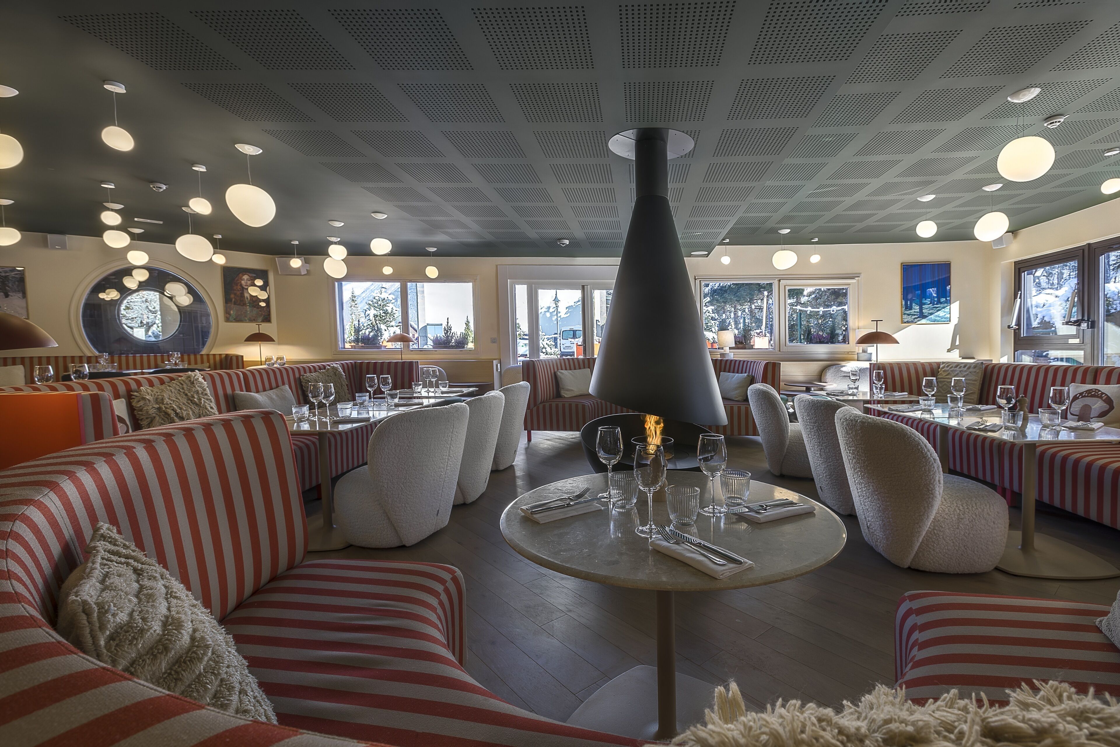 Un restaurant avec des sièges à rayures, des tables rondes et un foyer central.