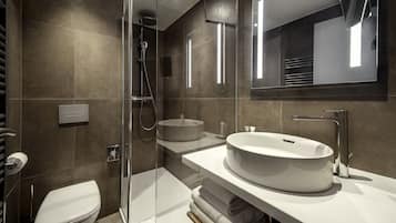 Un baño moderno con ducha de vidrio, un lavabo redondo y un espejo grande.