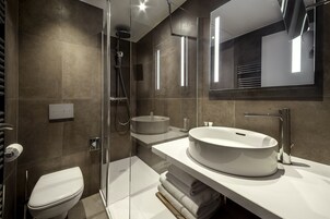 Un baño moderno con ducha de vidrio, un lavabo redondo y un espejo grande.