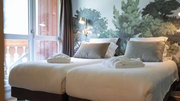 A hotel room with two beds, a large window, and a wall mural of trees.