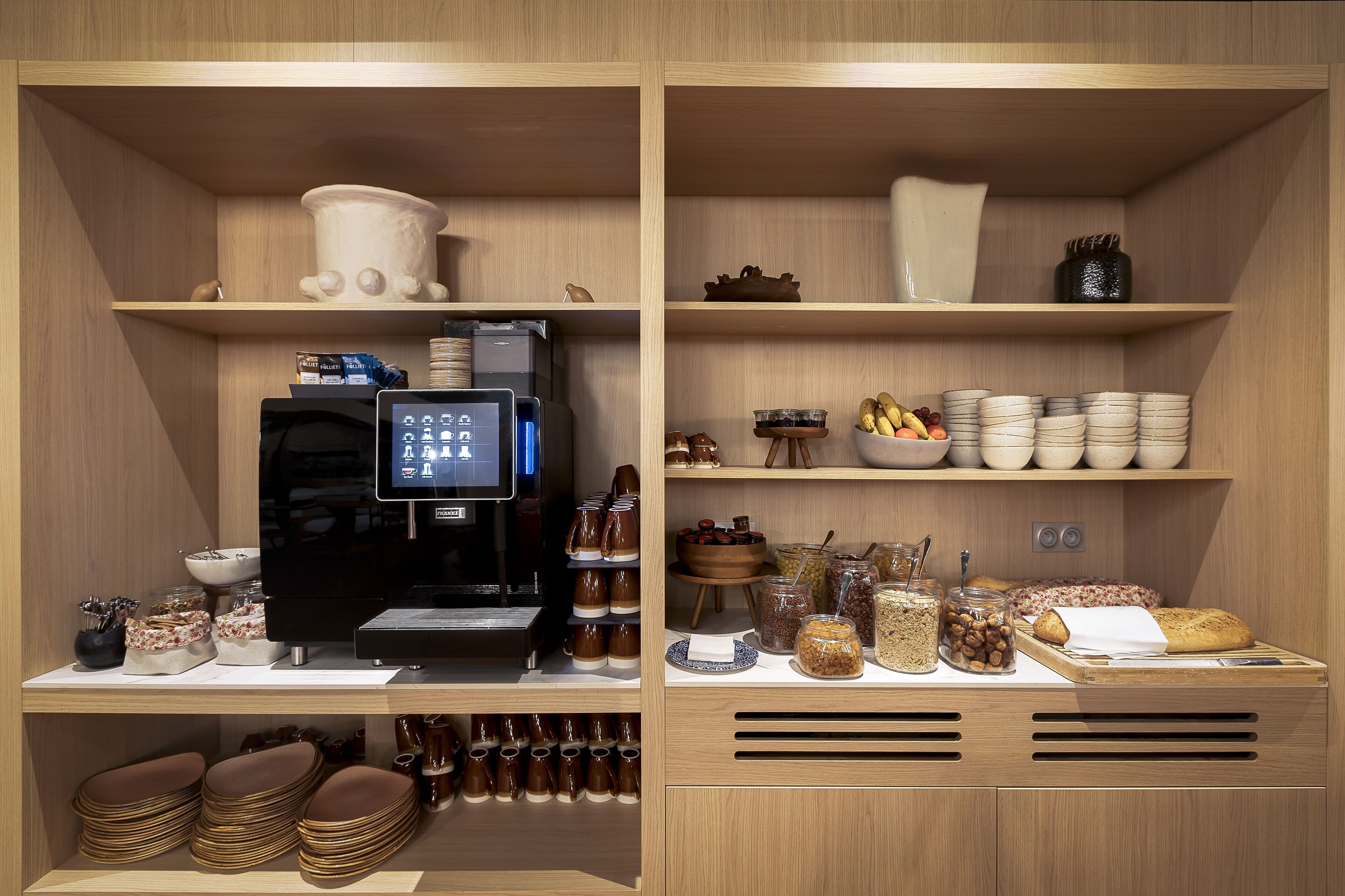 A kitchen area with a coffee machine, bowls, jars, and stacked plates.