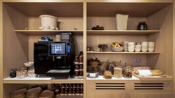 Una zona de cocina con cafetera, tazones, frascos y platos apilados.
