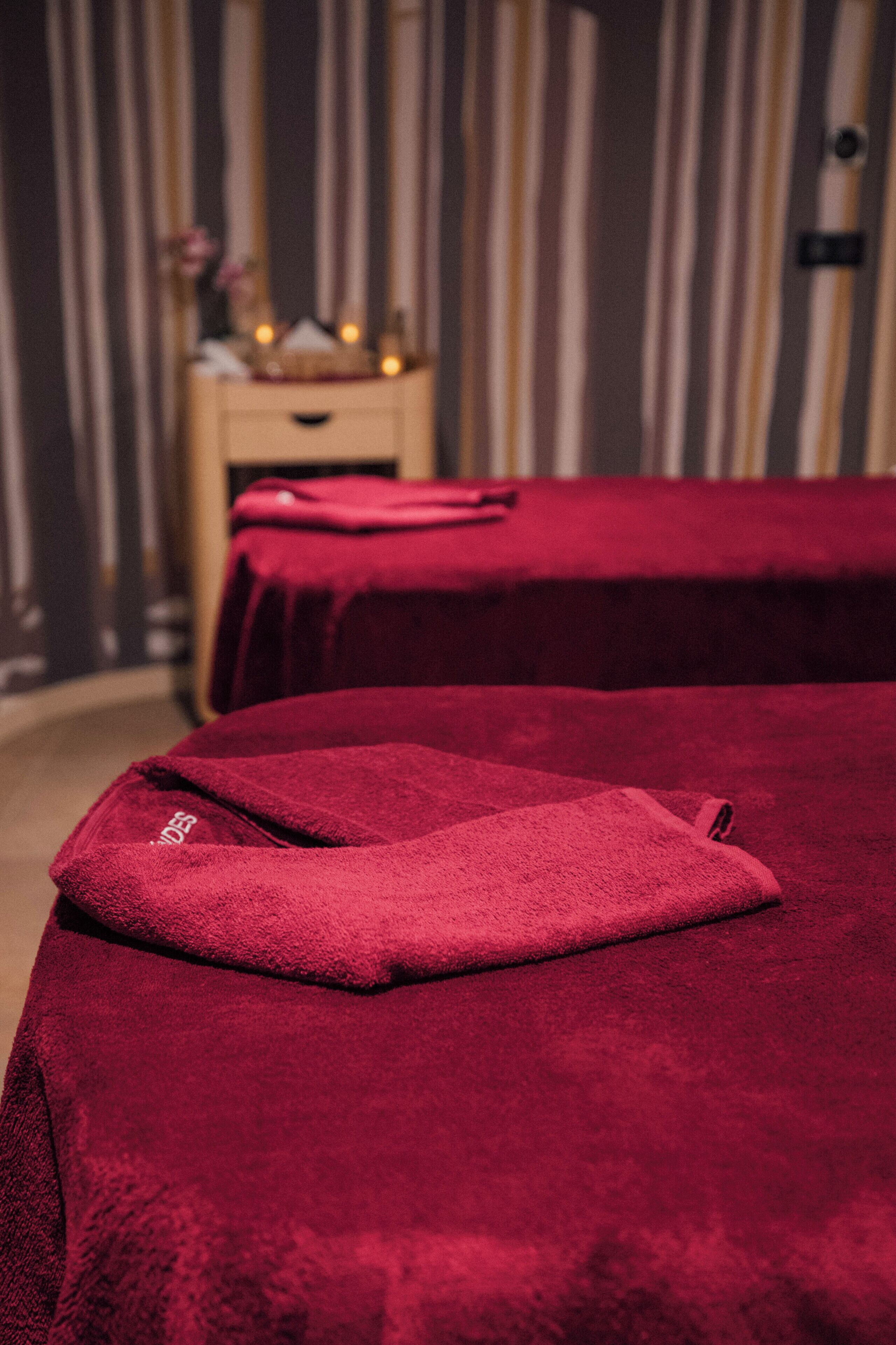 Une chambre avec deux lits recouverts de couvertures rouges, une table de chevet avec une lampe et, au fond, un rideau à rayures.