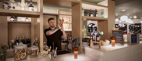 A bar area with shelves of liquor bottles, a bartender preparing a drink, and a chalkboard menu.